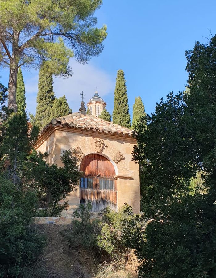 La ermita del calvario de Alloza, de piedra y con la puerta de madera, entre pinos y cipreses